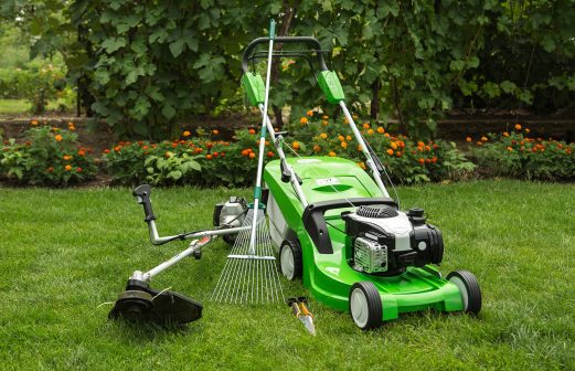 Green lawnmower, weed trimmer, rake and secateurs in the garden.